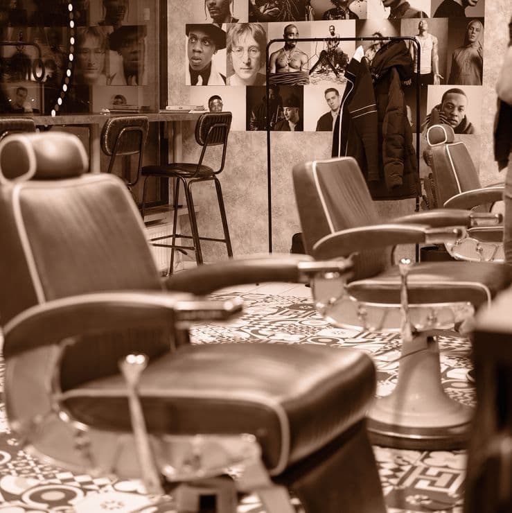 Barberarstolar i rad framför väggen med porträttbilder i salongen